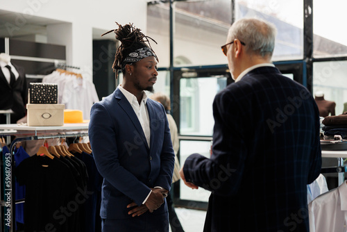 Stylish client discussing clothes fabric with store manager, looking to buy formal wear in shopping centre. Senior man buying fashionable merchandise to increase wardrobe in showroom. Fashion concept