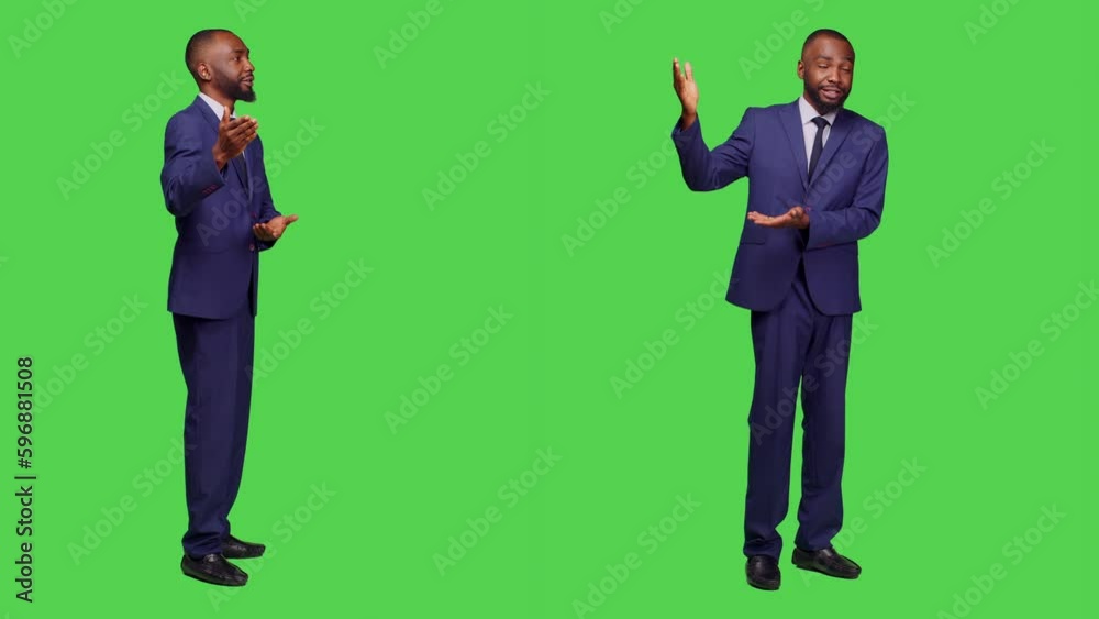 Businessman in office suit pointing sideways on camera, creating corporate presentation over full body greenscreen backdrop. Young male employee showing advertisement in studio.