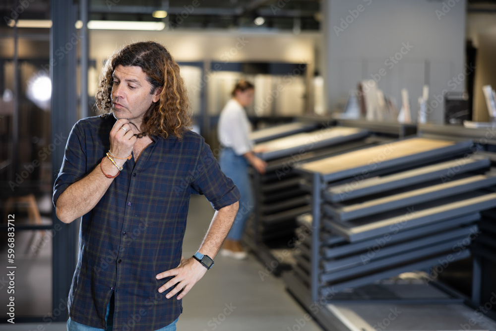 Fototapeta premium in hardware store, wistful man reflects on price-quality ratio of presented options for parquet flooring