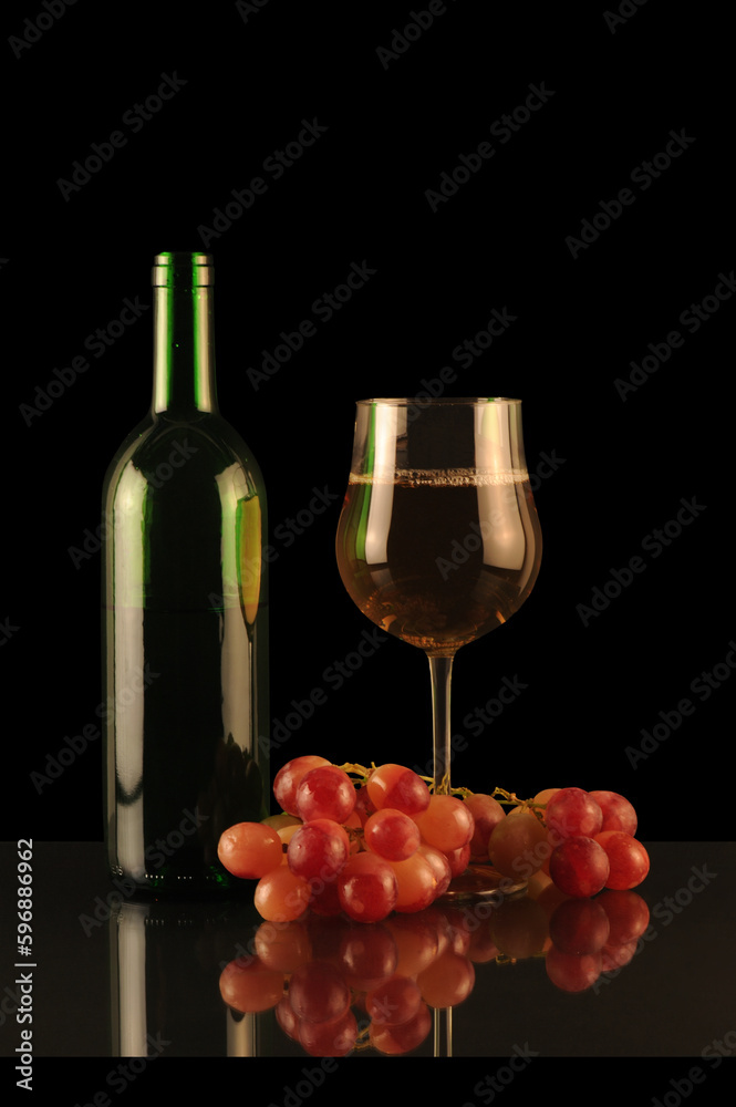 bottle and glass of white wine with grapes on a black background