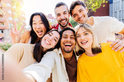 Happy group of diverse millennial friends taking selfie portrait together using mobile phone app. Multi ethnic teenage people having fun in city street. Friendship and youth lifestyle concept