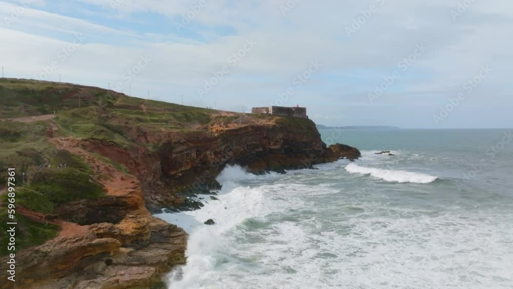 Epic aerial view of big waves of Nazare crashing on rocks with a lighthouse perched on the edge of a cliff in Portugal Epic aerial view of big waves of Nazare crashing on rocks with a lighthouse perched on the edge of a cliff in Portugal