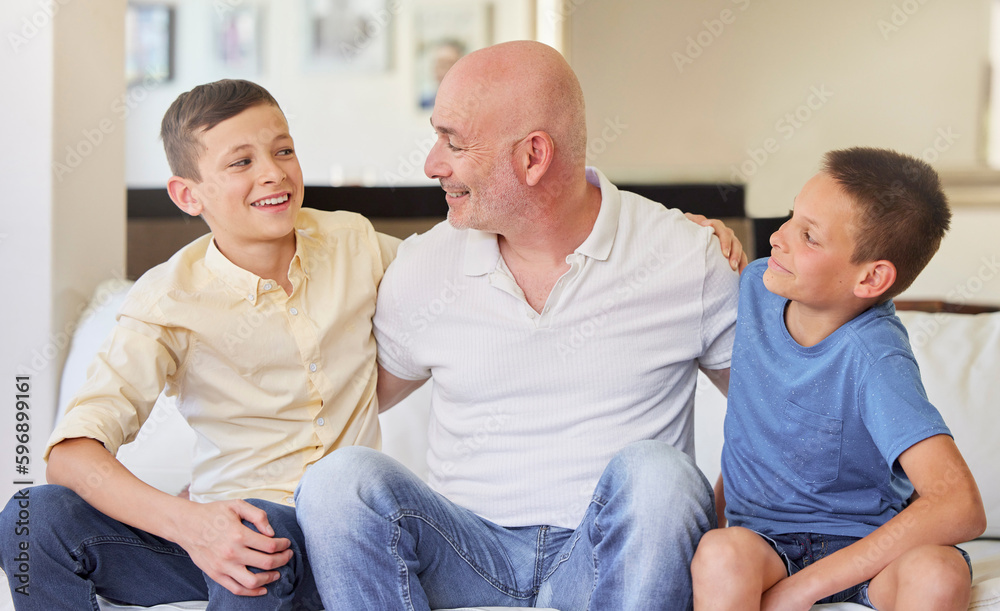 Caucasian man and his two sons sitting on the sofa at home. Happy family of three in the living room. Two brothers sitting with their dad. Smiling, bonding and spending quality time together Caucasian man and his two sons sitting on the sofa at home. Happy family of three in the living room. Two brothers sitting with their dad. Smiling, bonding and spending quality time together