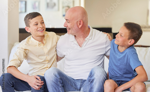Caucasian man and his two sons sitting on the sofa at home. Happy family of three in the living room. Two brothers sitting with their dad. Smiling, bonding and spending quality time together © Jade M/peopleimages.com