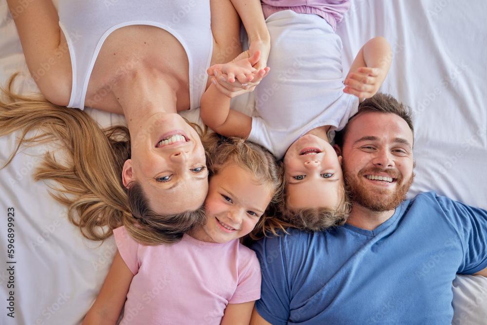 Above happy parents with little children lying on a bed at home and looking up. Caucasian girls bonding with their mother and father. Smiling young married couple enjoying free time with daughters Above happy parents with little children lying on a bed at home and looking up. Caucasian girls bonding with their mother and father. Smiling young married couple enjoying free time with daughters