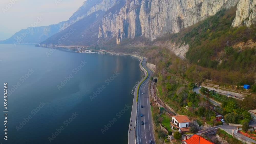 Aerial view of a beautiful european city near the shore of freshwater lake como in lombardy. Gothic church bell tower. Roofs of buildings. Mountains and rocks. Road by the water. Lecco Italy 11.2023