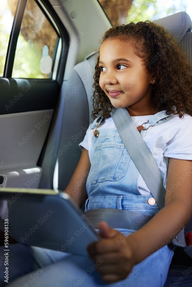 Shes got everything she needs for the trip. Cropped shot of an adorable little girl using her tablet while sitting in the backseat of a car.