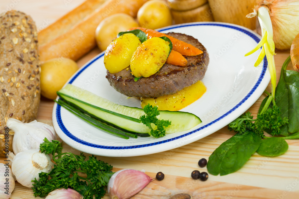 Appetizing beef cutlet with baked new potatoes and carrots garnished with fresh cucumber and greens