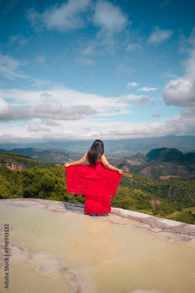 Mujer con vestido rojo junto a lago con montañas al fondo en Hierve el agua, Oaxaca