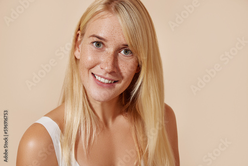 Beautiful young female with smooth freckled skin. Woman with blond hair and perfect skin against a pastel background.