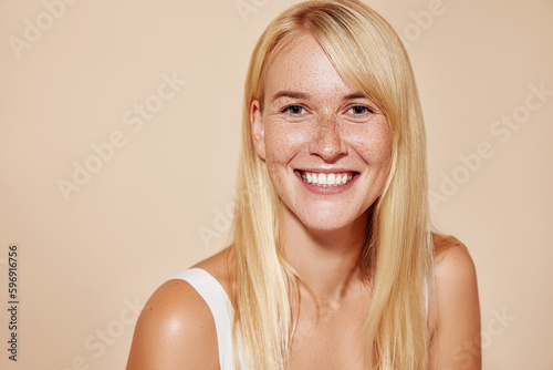 Cheerful blond female with perfect smooth skin looking at camera. Portrait of a happy freckled woman looking straight at a camera.
