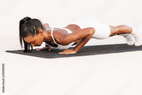 Slim muscular woman doing push-ups on a mat in the white outdoor studio. Professional athlete exercising on a mat doing a core workout.