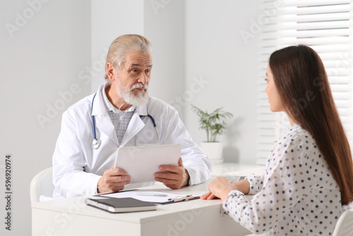 Senior doctor consulting patient at white table in clinic