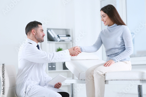 Happy doctor shaking hands with patient in hospital