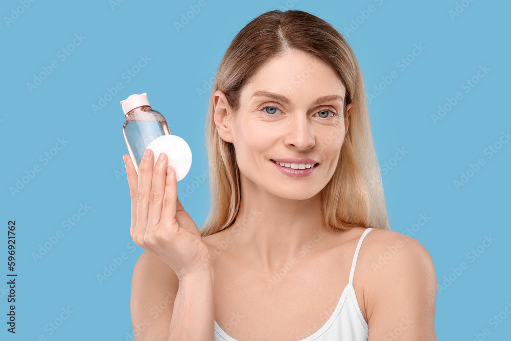 Beautiful woman with makeup remover and cotton pad on light blue background Beautiful woman with makeup remover and cotton pad on light blue background