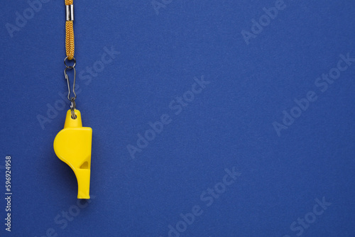 One yellow whistle with cord on blue background, top view. Space for text photo