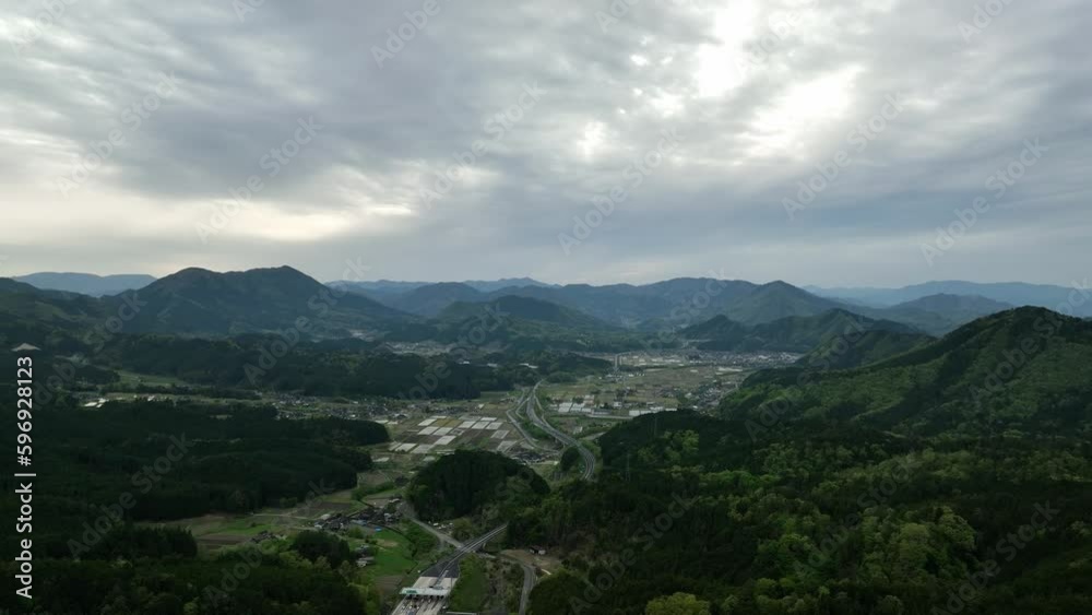 Flyover small town in rural Japan with green mountain landscape on cloudy day Flyover small town in rural Japan with green mountain landscape on cloudy day