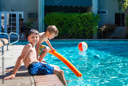 Oudoor summer activity. Concept of fun, health and vacation. Brothers boys eight and five years old with noodle sits near a pool in hot summer day.