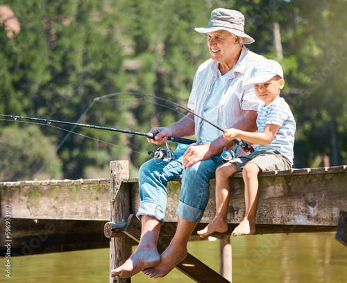 A hobby that he will grow up loving. Shot of a little boy fishing with his grandfather at a lake in a forest.
