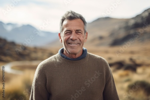 Portrait of happy senior man standing outdoors in the countryside. He is looking at camera and smiling.