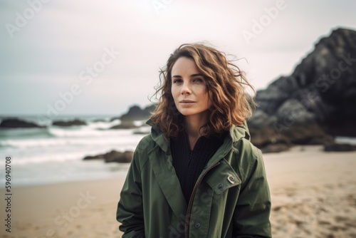 Portrait of a beautiful young woman with curly hair in a green coat on the beach