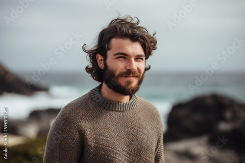 Portrait of handsome young man with long curly hair wearing warm sweater at the beach
