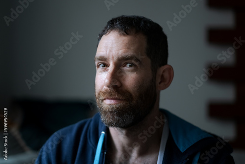 A bearded man expresses relaxation and the feeling of staying at home. His casual blue hoodie is unzipped, showing his chest hair.