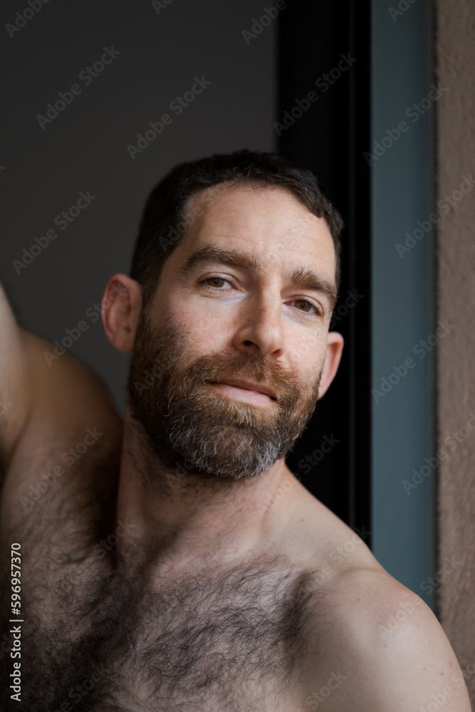 Lifting up his arms, a man expresses happiness, strength, and confidence. He is shirtless, with a thick beard that draws attention to his face. Lifting up his arms, a man expresses happiness, strength, and confidence. He is shirtless, with a thick beard that draws attention to his face.
