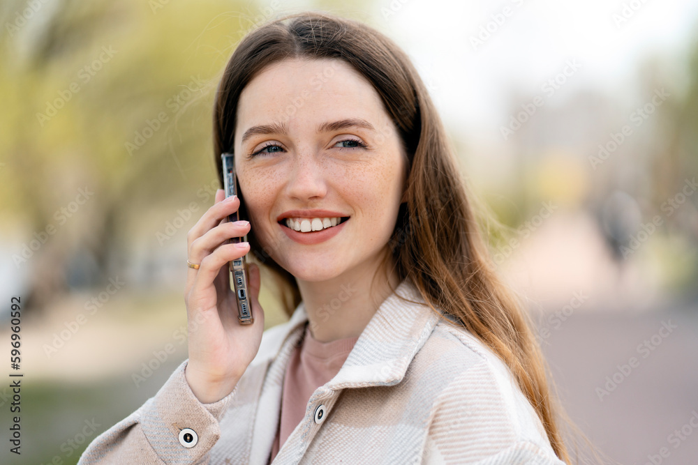 Young beautiful smiling woman talking on mobile phone looking away standing on the street. Technology concept Young beautiful smiling woman talking on mobile phone looking away standing on the street. Technology concept