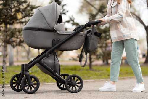 Cropped images of young pushing stroller with newborn baby inside, walking in spring park. Parenthood, healthy lifestyle concept 