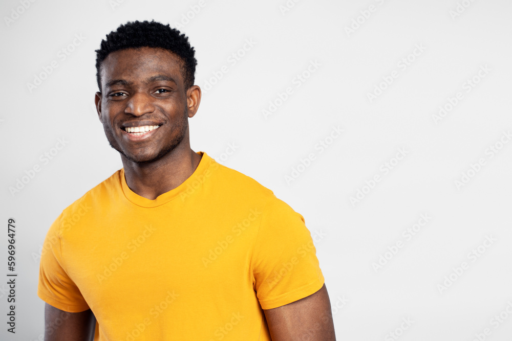 Closeup portrait of smiling confident African man wearing orange t shirt isolated on white background, copy space. Happy friendly Nigerian student looking at camera, education concept