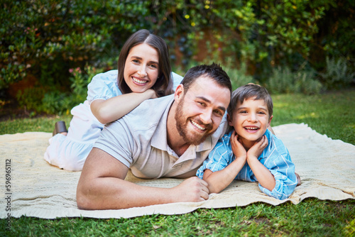Portrait of a happy caucasian family lying on a picnic blanket in the garden. Smiling family bonding, being affectionate outside while enjoying the day. Little boy relaxing with his parents © Lumeez I/peopleimages.com