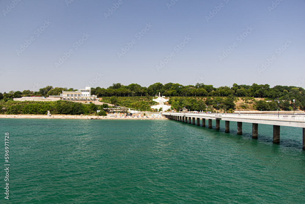 Coastline of a small town with a white pier and green trees. View from the sea