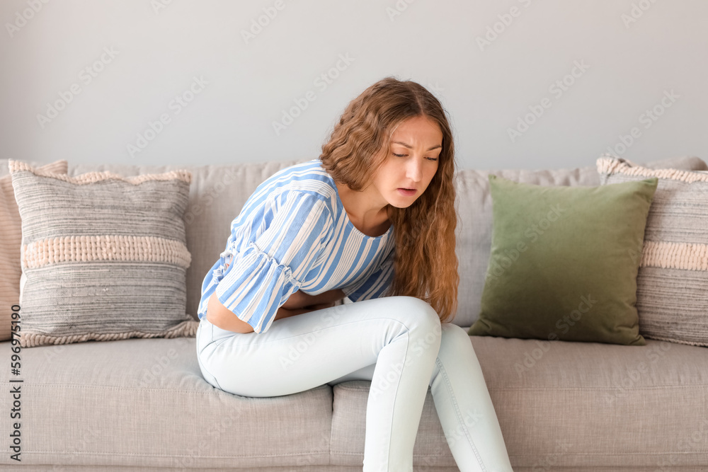 Young woman with appendicitis sitting on sofa at home