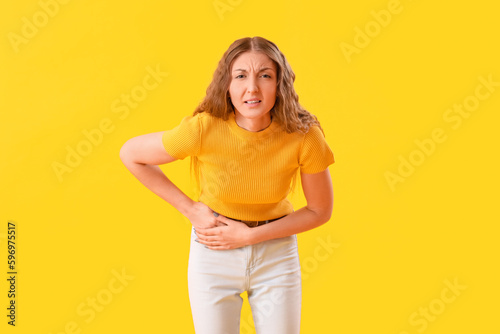 Young woman with appendicitis on yellow background