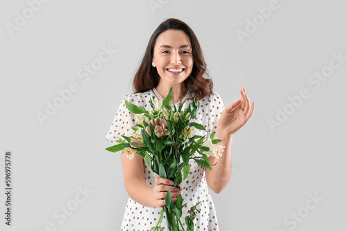 Young woman in dress with alstroemeria flowers on grey background photo