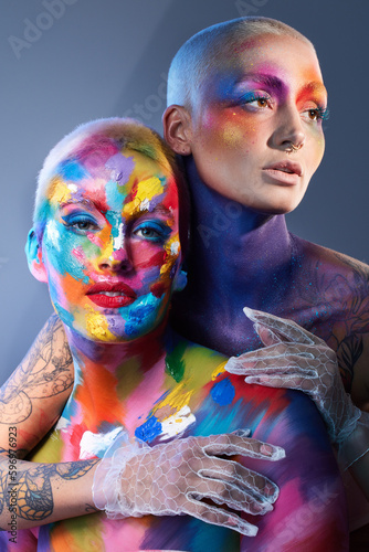 We see the world in technicolour. Studio shot of two young women posing with multi-coloured paint on her face. photo