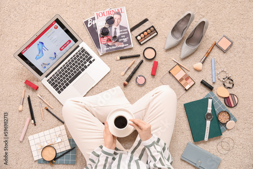 Woman with cup of coffee, laptop and accessories shopping online on beige carpet
