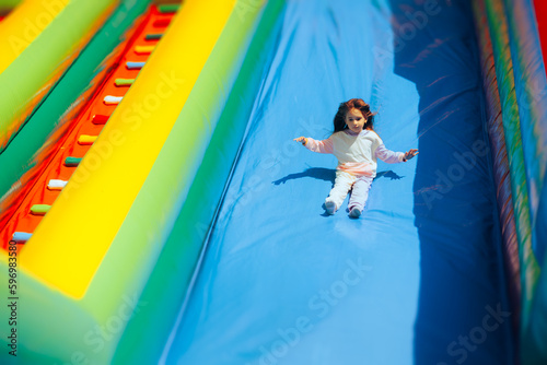 Happy Girl Playing on a Huge Inflatable Slide in Amusement Park. Cheerful carefree child having fun in a bouncing castle 

 photo