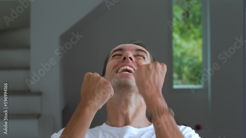 Happy male winner celebrating victory, making funny jumping and showing Yes gesture on home background. Young lucky man 30s emotionally celebrating win, showing positive emotions. Winning concept.