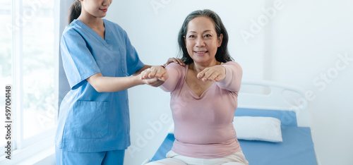 Asian Chinese female physiotherapist caregiver helping elderly woman exercise for recovery, prevention of osteoarthritis and osteoporosis.