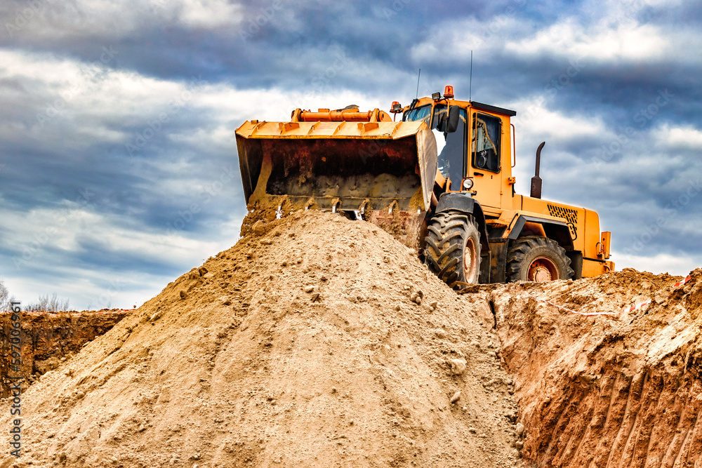 Powerful wheel loader or bulldozer working on a quarry or construction site. Loader with a full bucket of sand against the sky. Powerful modern equipment for earthworks.