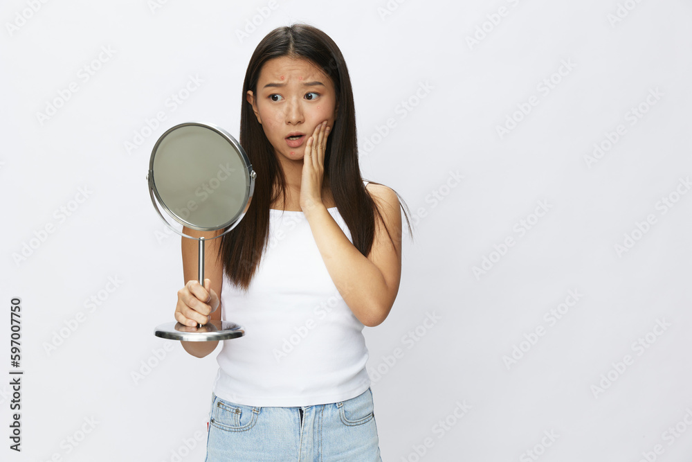 Asian woman with mirror in hand facial skin problems, acne and inflammation, red rash and allergies, chicken pox, sadness from rashes. Facial skin care concept for diseases and nerves Asian woman with mirror in hand facial skin problems, acne and inflammation, red rash and allergies, chicken pox, sadness from rashes. Facial skin care concept for diseases and nerves
