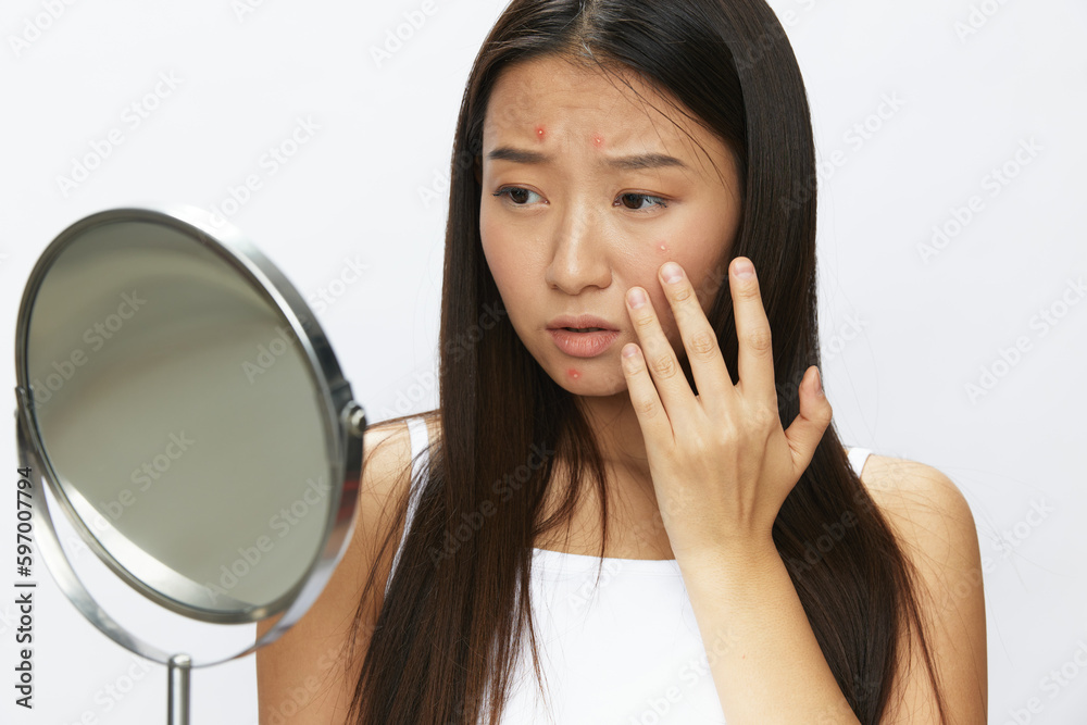 Asian woman with mirror in hand facial skin problems, acne and inflammation, red rash and allergies, chicken pox, sadness from rashes. Facial skin care concept for diseases and nerves Asian woman with mirror in hand facial skin problems, acne and inflammation, red rash and allergies, chicken pox, sadness from rashes. Facial skin care concept for diseases and nerves