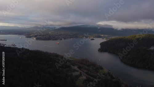 Pan up to ocean bay next to mountains with cities along the shore during a cloudy evening in Vancouver, BC