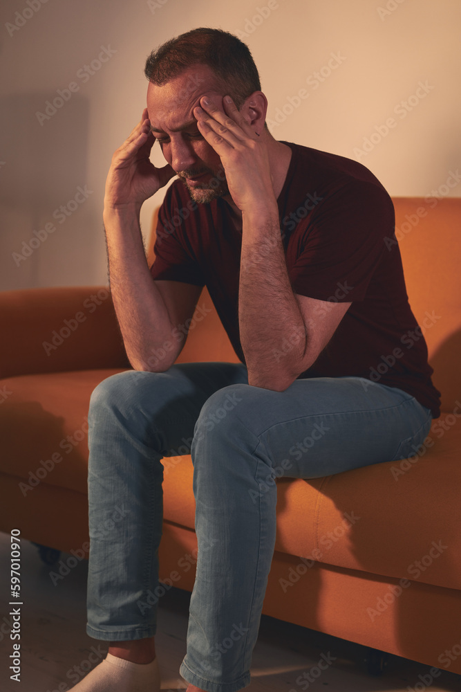 Man with headache sitting on a sofa at home. Man with headache sitting on a sofa at home.