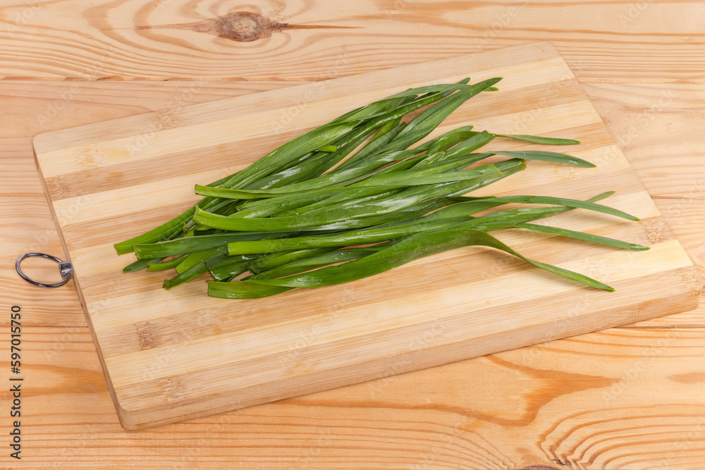 Green stems of garlic on cutting board on rustic table Green stems of garlic on cutting board on rustic table
