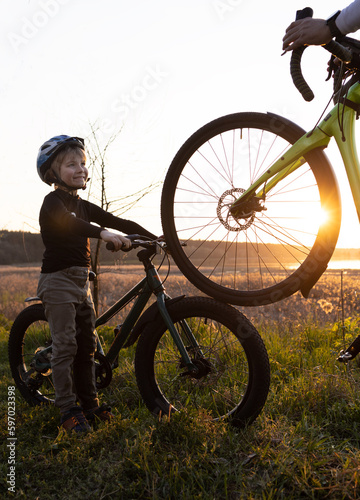 Silhouette of an adult and children's bicycles and a boy in a helmet in the rays of the back sun. Family vacation, cycling, travel, healthy lifestyle. leisure. father's day, son's day