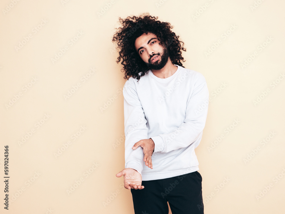 Handsome smiling hipster model. Unshaven Arabian man dressed in white summer sweater and trousers clothes. Fashion male with long curly hairstyle posing near wall. Isolated. Copy space, mockup Handsome smiling hipster model. Unshaven Arabian man dressed in white summer sweater and trousers clothes. Fashion male with long curly hairstyle posing near wall. Isolated. Copy space, mockup
