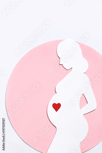 Paper silhouette of a pregnant woman in a pink circle on a white background. Vertical image, flat lay, copy space.